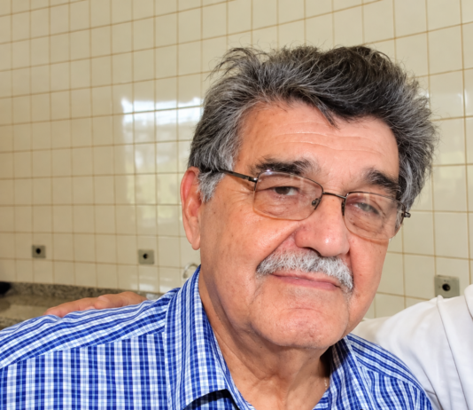 Retrato do jornalista João Natalício de Oliveira, de Ponta Porã, com óculos e camisa azul xadrez; imagem aprimorada digitalmente