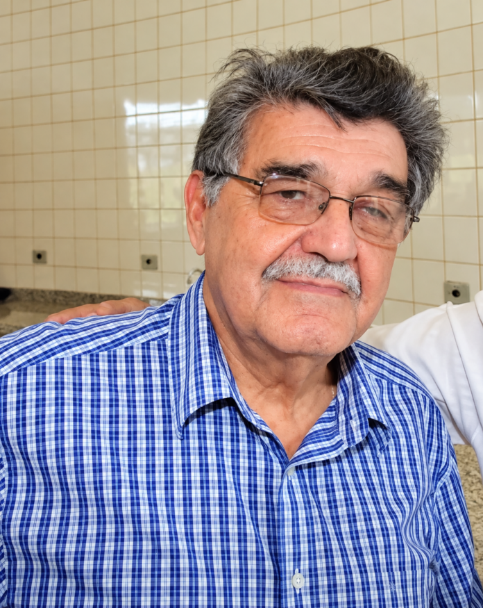Retrato do jornalista João Natalício de Oliveira, de Ponta Porã, com óculos e camisa azul xadrez; imagem aprimorada digitalmente