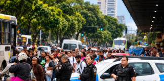 Imagem ilustrativa gerada por inteligência artificial de policiais militares, viatura e multidão em via urbana, representando o debate sobre segurança pública nas eleições de 2026