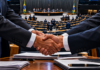 Ilustração de aperto de mãos em primeiro plano com o plenário da Câmara dos Deputados ao fundo, representando articulações partidárias